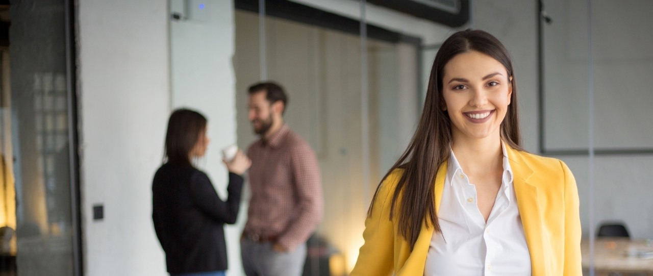 Portrait of successful business woman standing with her colleagues standing in background at office.